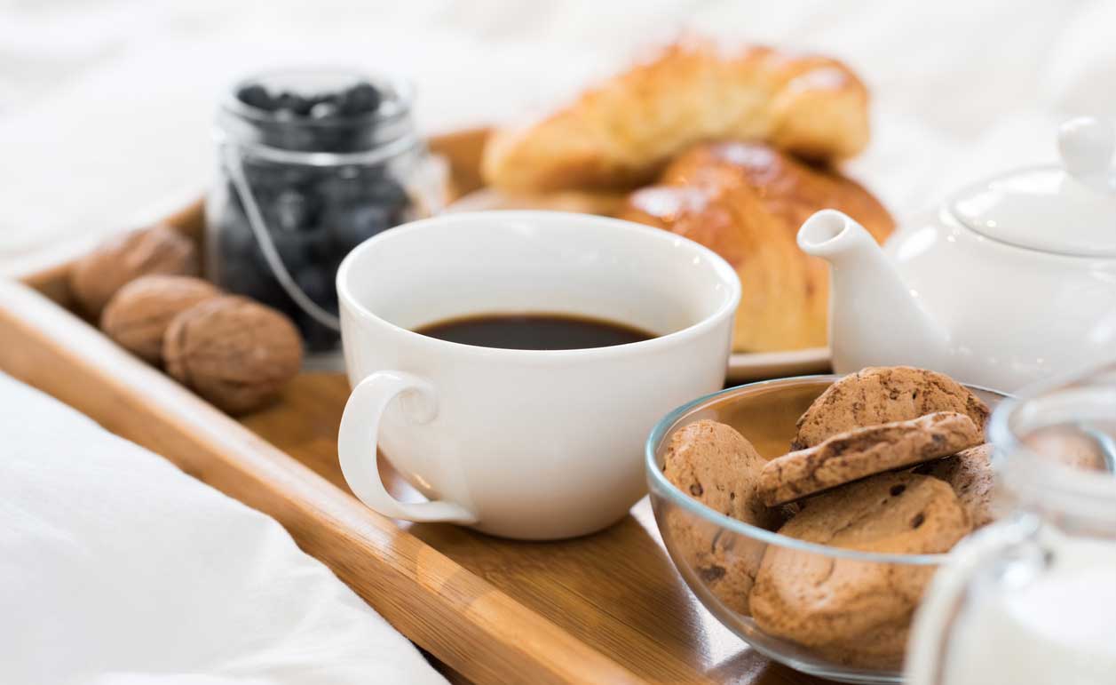 Ontbijt dienblad met koffie, croissants, koekjes, bessen en melk op een tafel.