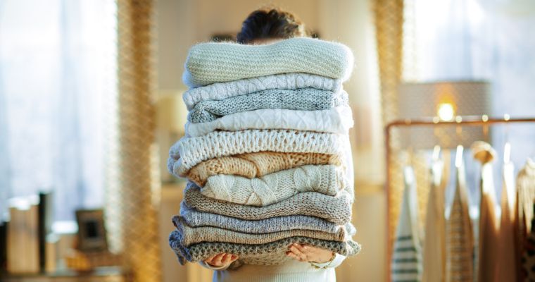 Vrouw houdt stapel truien vast voor opslag